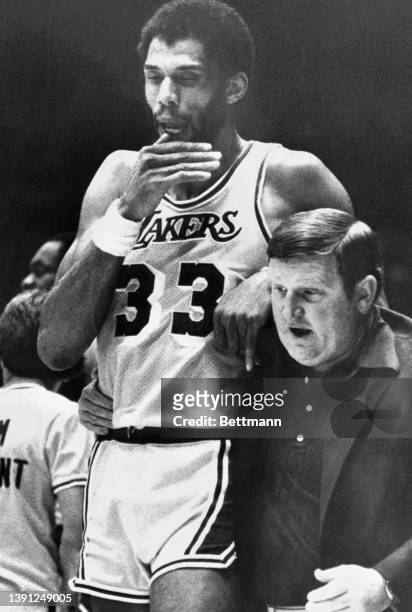 Kareem Abdul-Jabbar with ankle injury of the Los Angeles Lakers grimaces as he is helped off the floor by the team trainer after hurting his ankle...