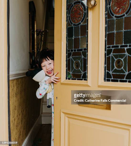 a cute little girl peeks around a front door and smiles - answering stock-fotos und bilder