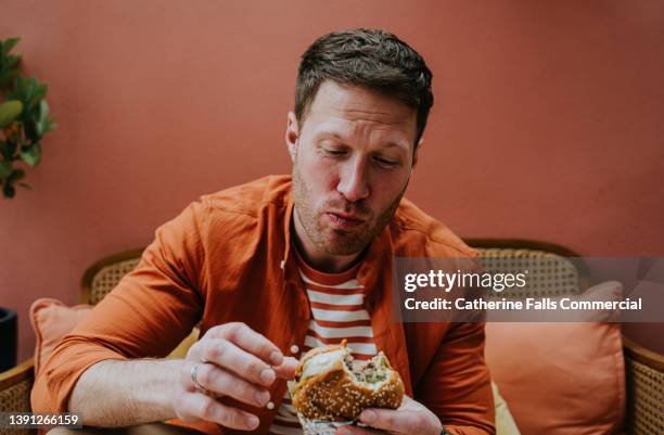 a man chews a large bite of a burger - morder imagens e fotografias de stock