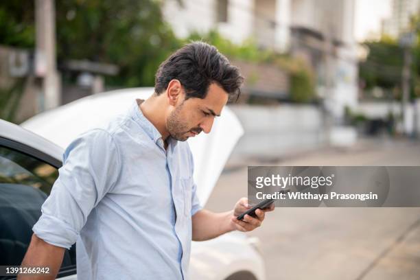 young man is text messaging, standing next to a broken down car - asian waiting angry expressions stock pictures, royalty-free photos & images