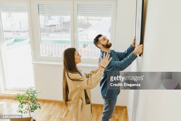 pareja joven arreglando nuevo piso, colgando pintura, nuevo hogar y concepto de reubicación. - draped fotografías e imágenes de stock