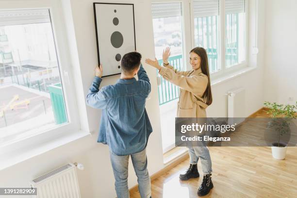 young couple arranging new flat, hanging up painting, new home and relocation concept. - move to new place stock pictures, royalty-free photos & images