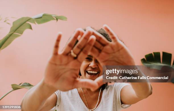 a young woman holds her palms up towards the camera and smiles through the gap in her hands - woman reaching hands towards camera stock-fotos und bilder