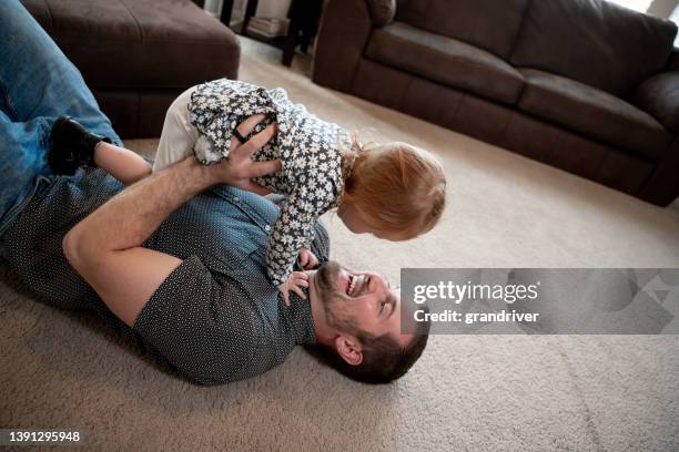 2歳の娘を持つ若い父親が抱擁し、住宅のリビングルームのカーペットで遊んでいる - 2 year old blonde girl father ストックフォトと画像