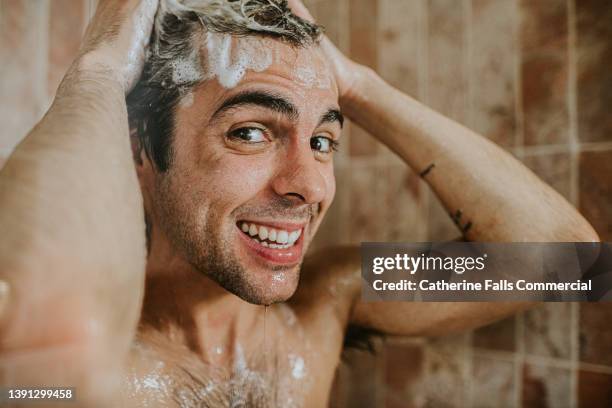 a man washes his hair in the shower. he is confident and happy as he smiles into the camera. - hot body pic stock pictures, royalty-free photos & images