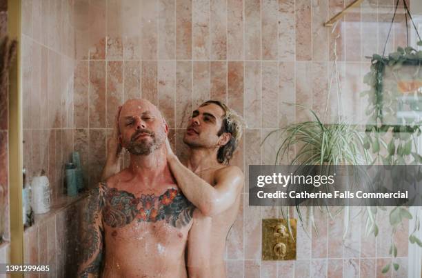 a gay couple enjoy a romantic moment in the shower as one gives the other a head massage - gay by shower stock pictures, royalty-free photos & images