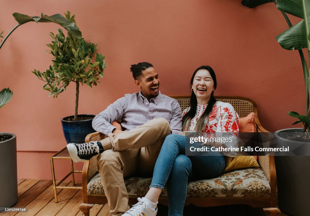 Two friends / young couple sit on a sofa and laugh together