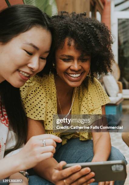 two young woman look at a phone screen and smile - happy smile with phone foto e immagini stock