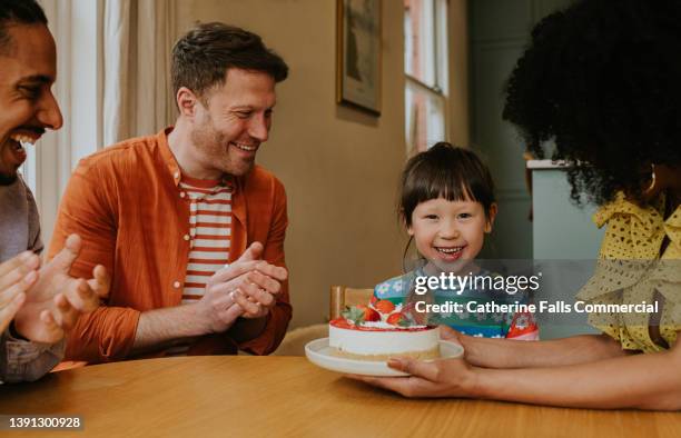 a little girl is presented with a strawberry cake and she looks delighted - adopted chinese daughter ストックフォトと画像