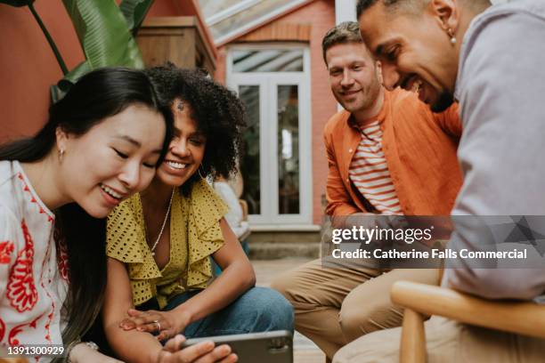 a group of 4 young people watch a video on a smart phone - female exhibitionist ストック��フォトと画像