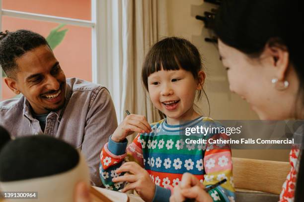 a man and a woman encourage a cute young girl as she draws on an artists easel. the child looks delighted. - chinese tutor study stock-fotos und bilder