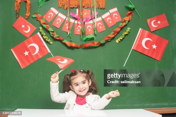 preschooler girl holding turkish flag in front of green chalkboard with national holiday ornaments. - april 5 stock pictures, royalty-free photos & images