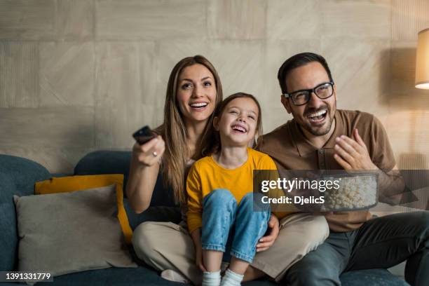 happy young family watching tv together at home. - tv family stockfoto's en -beelden