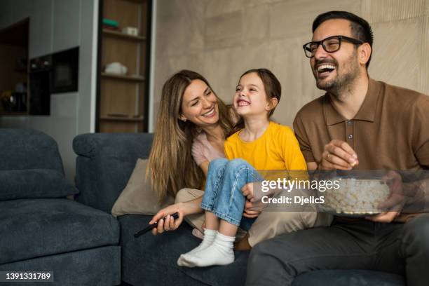 happy young family watching tv together at home. - tv family stockfoto's en -beelden