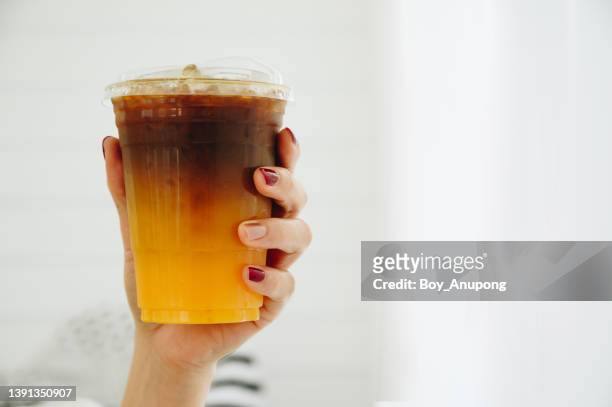 someone hand holding a cup of iced orange americano. - orange juice stock-fotos und bilder