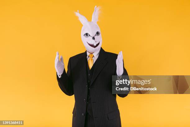 disguised person in rabbit mask wearing suit jacket, vest and tie, raising arms excited, on yellow background. carnival, party, easter and celebration concept. - easter bunny suit stock pictures, royalty-free photos & images