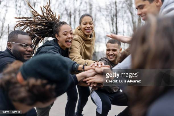 cheerful young male and female football players stacking hands together - community togetherness stock pictures, royalty-free photos & images