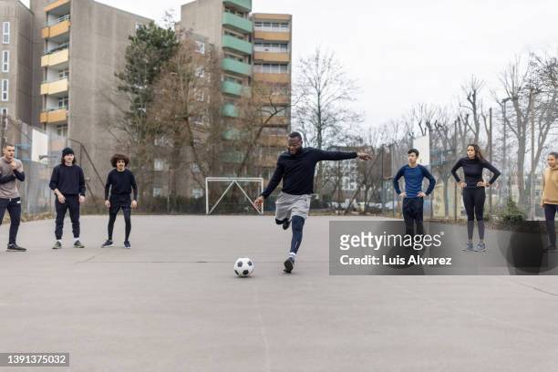 group of men and women playing soccer on urban playground - strafstoß serie fußball und andere sportarten stock-fotos und bilder