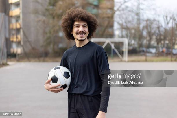 smiling young man holding soccer ball in street court - 1 etappe stock-fotos und bilder