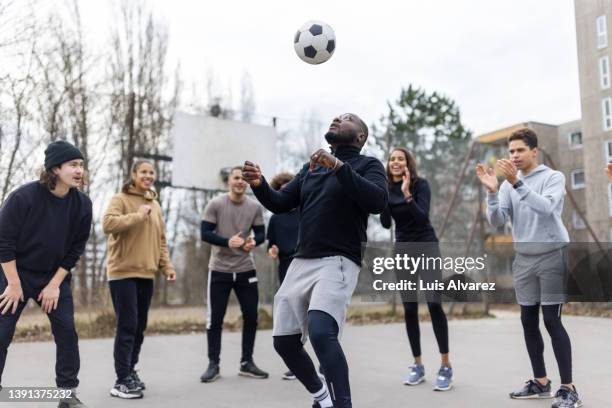 african man juggles football in center with friends standing in circle - street games stock pictures, royalty-free photos & images