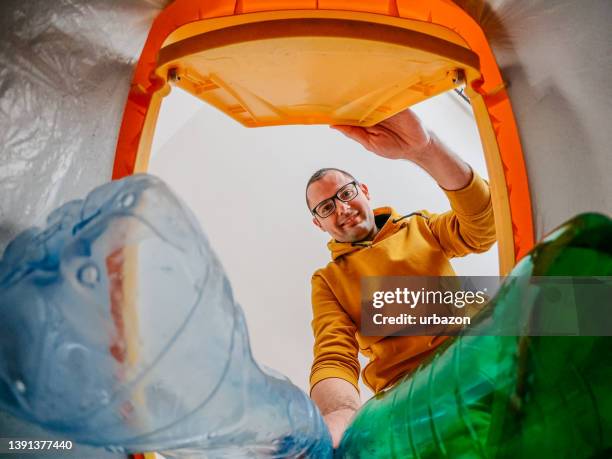 young man puts plastic bottles into recycling bin - lata de lixo imagens e fotografias de stock