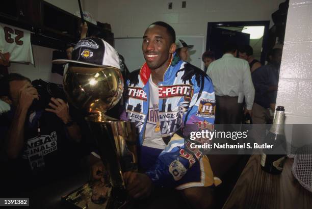 Guard Kobe Bryant of the Los Angeles Lakers smiles as he holds the championship trophy in the locker room after winning Game Four of the 2002 NBA...