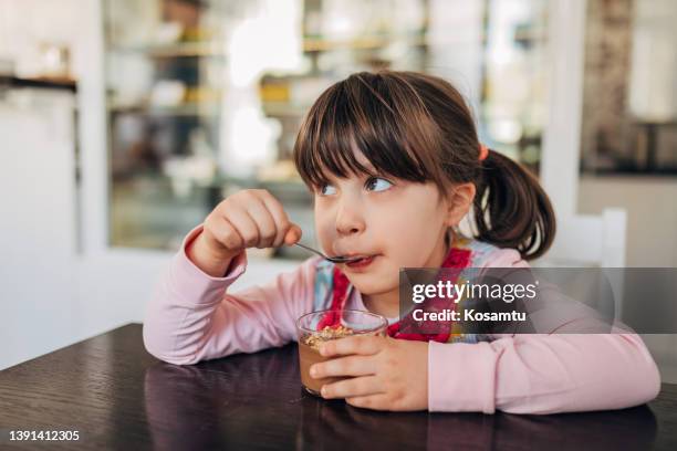 una bambina carina si diverte a mangiare la sua mousse al cioccolato preferita in un bicchiere, da una pasticceria - mousse foto e immagini stock