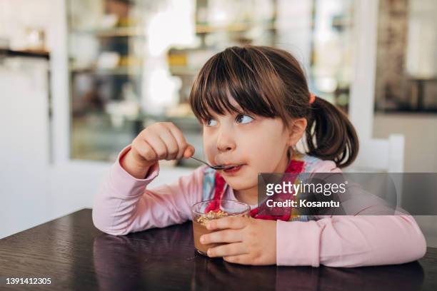 a cute little girl enjoys eating her favorite chocolate mousse in a glass, from a pastry shop - chocolate pudding imagens e fotografias de stock