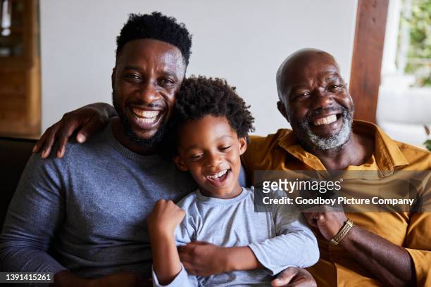 man and his senior dad and young son laughing together on a sofa - black father stock pictures, royalty-free photos & images