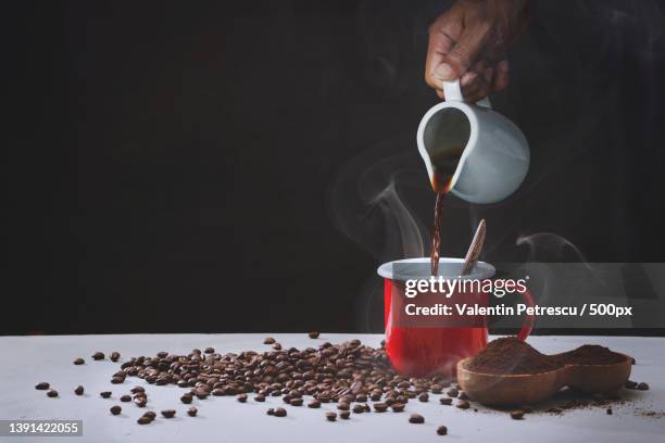 cropped hand pouring coffee in cup on table against black background - koffeinmolekül stock-fotos und bilder