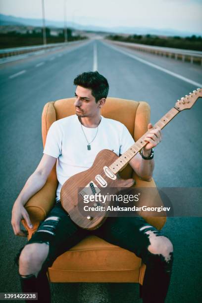 guitarrista relajándose en la silla en medio de la carretera con la guitarra en la mano - guitar case fotografías e imágenes de stock
