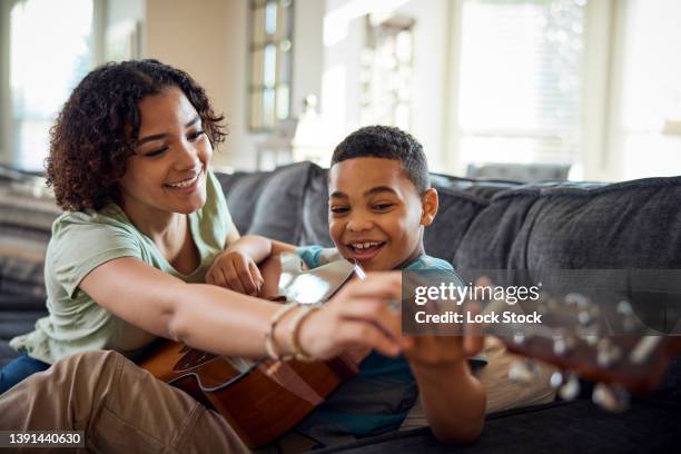 teenage girl teaches her brother guitar on the sofa. - songwriter - fotografias e filmes do acervo