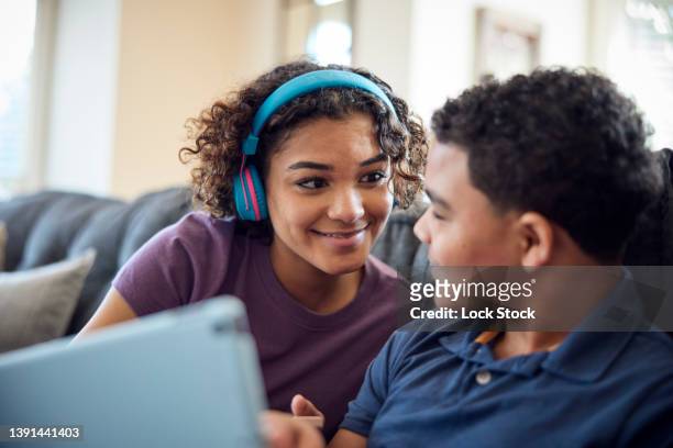 sister and brother look at tablet on the sofa together in the living room. - sister stock photos et images de collection