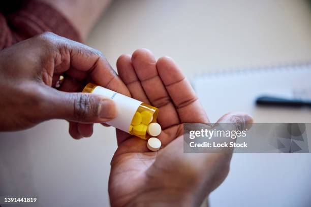 african american man pouring medications out of a bottle into his hand. - healthcare and medicine foto e immagini stock