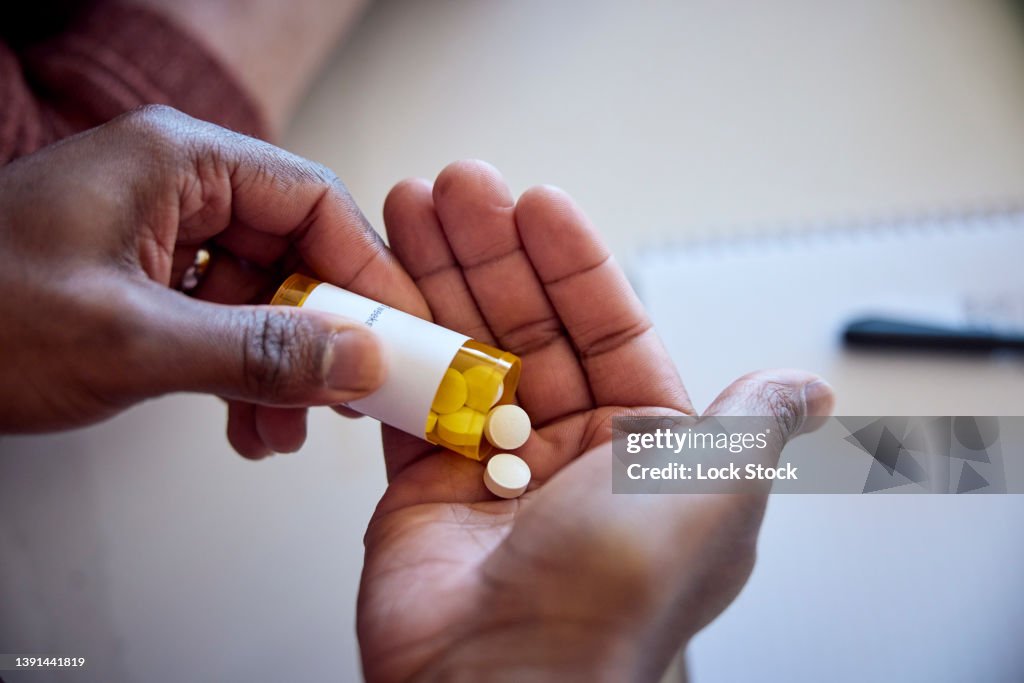 African American man pouring medications out of a bottle into his hand.