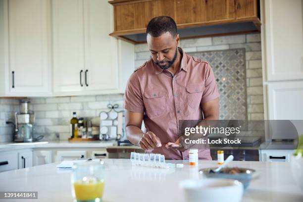 african american man putting medications in a daily pill organizer - contenitore organizer per pillole foto e immagini stock