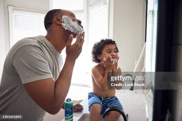 young african american watching his father shave in the bathroom mirror. - shaving cream stock-fotos und bilder