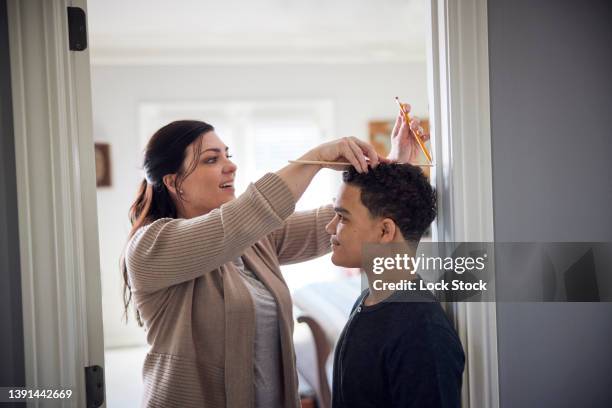 caucasian mother measuring height of mixed-race son on wall. - groeimeter stockfoto's en -beelden