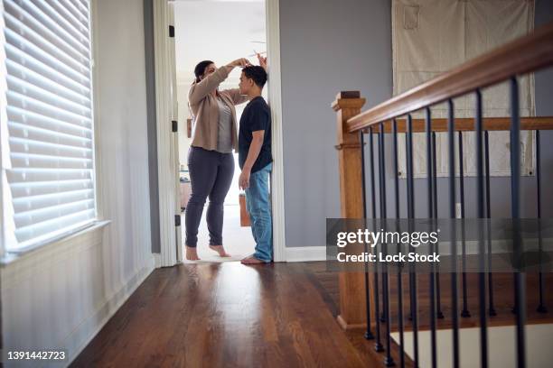 caucasian mother measuring height of mixed-race son on wall. - height chart stock pictures, royalty-free photos & images