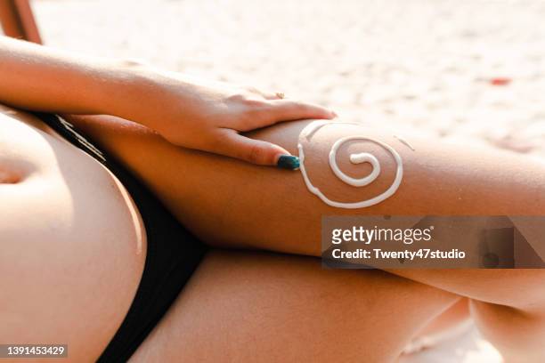 close up a woman in bikini applying suntan lotion on the leg - suntan lotion stock-fotos und bilder