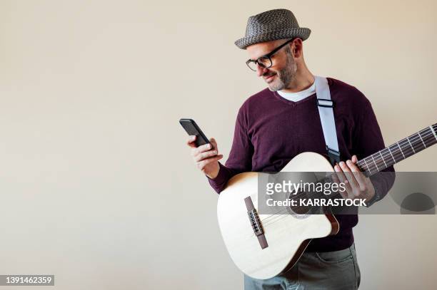 man using smart phone and holding an electroacoustic guitar. - plucking an instrument foto e immagini stock