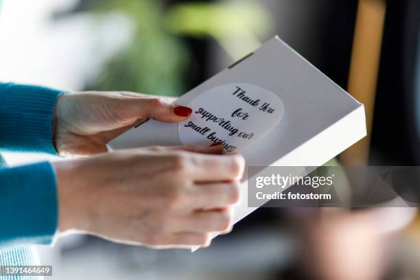 unrecognizable female entrepreneur applying a ''thank you'' label on a package - etiketteren stockfoto's en -beelden