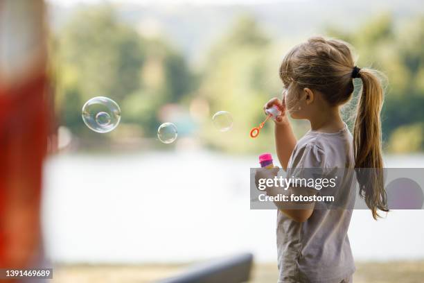 side view of cute little girl blowing soap bubbles outside - bubble ponytail stock pictures, royalty-free photos & images