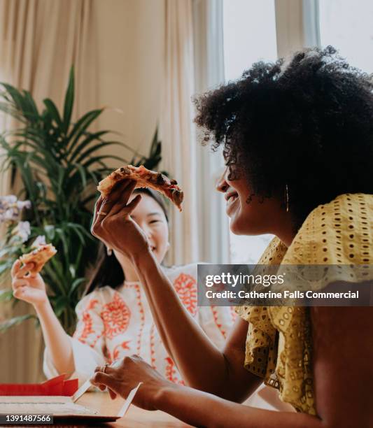 a woman enjoys a slice of pizza with a friend - cheese pull stockfoto's en -beelden