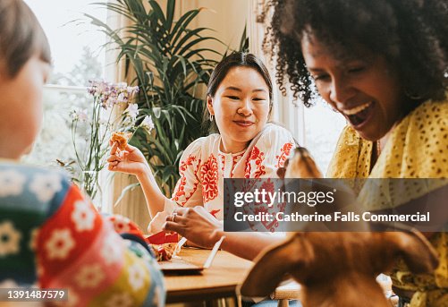 A woman looks amused as a friend gives in and gives a mischievous dog a little bit of pizza from the table A woman looks amused as a friend gives in and gives a mischievous dog a little bit of pizza from the table