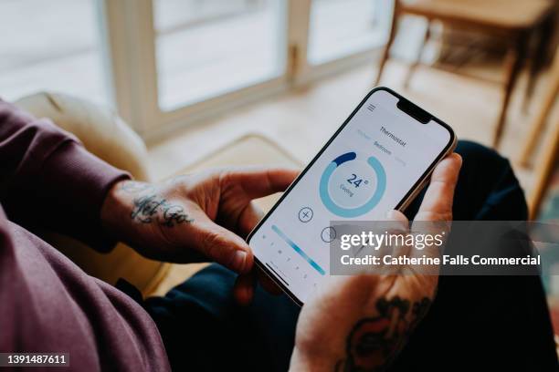 a man controls a thermostat with an app on his mobile device - temperature control stock pictures, royalty-free photos & images