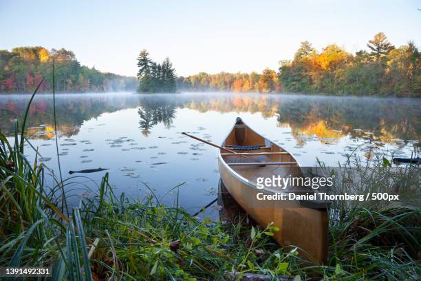 canoe on shore of calm lake with island at sunrise during autumn - brainerd photos et images de collection
