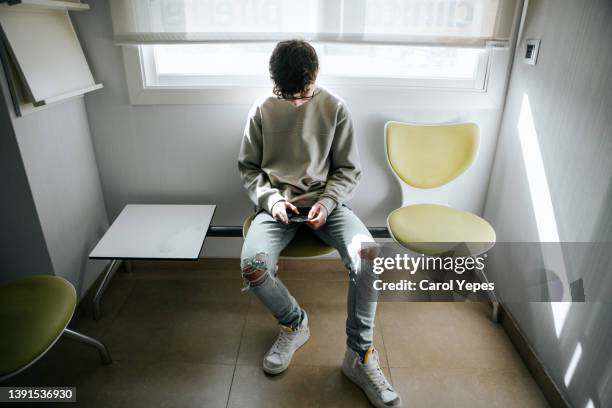 teenager sitting in medical waiting room and using mobile phone - arztstuhl stock-fotos und bilder