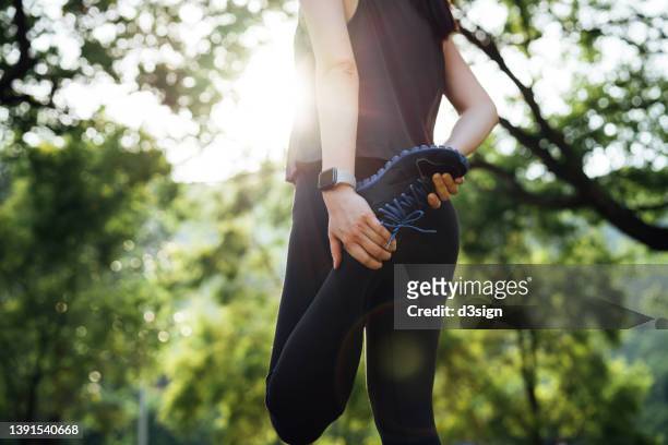 cropped shot of young asian sports woman stretching her legs before going for a run in green park outdoors with sunlight in morning. health and fitness training, healthy living lifestyle, sports routine concept - leg show fotografías e imágenes de stock