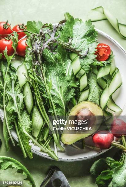 healthy salad ingredients : green lettuce, avocado, tomatoes, radish, cucumber and herbs at white plate on kitchen table - green salad foto e immagini stock